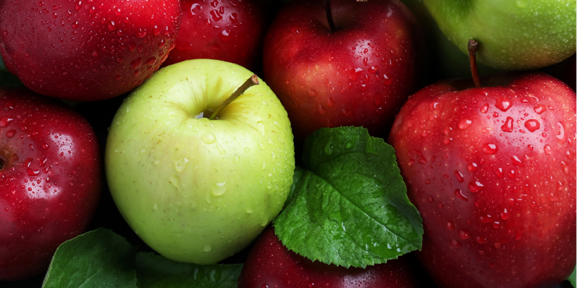 Maçãs vermelhas e verdes frescas com gotas de água e folhas verdes agrupadas.