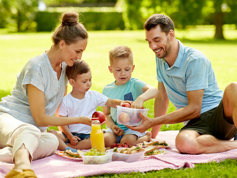 family, leisure and people concept - happy mother, father and two little sons having picnic at summer park