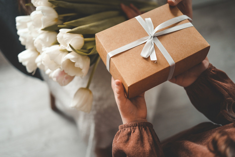 The child's hands hold a beautiful gift box with a ribbon and white tulips. Top view, close-up. Happy mother's day.