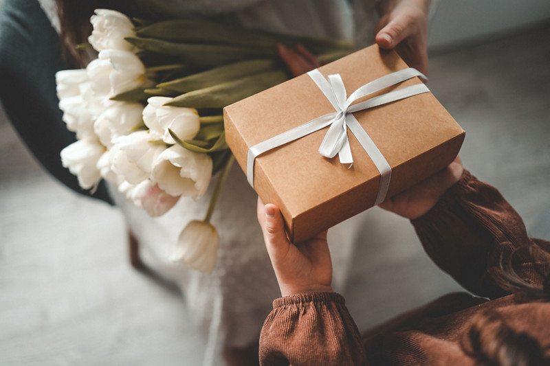 The child's hands hold a beautiful gift box with a ribbon and white tulips. Top view, close-up. Happy mother's day.