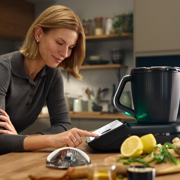 Mulher usa Bimby TM7 e Mandolina Bimby na cozinha com ingredientes na mesa