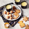 Prato com bolachas decoradas trufas de chocolate três chávenas de bebida cremosa vela e guardanapo sobre mesa de mármore