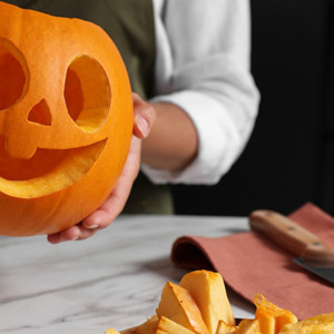 Woman holding carved pumpkin for Halloween at white marble table, closeup