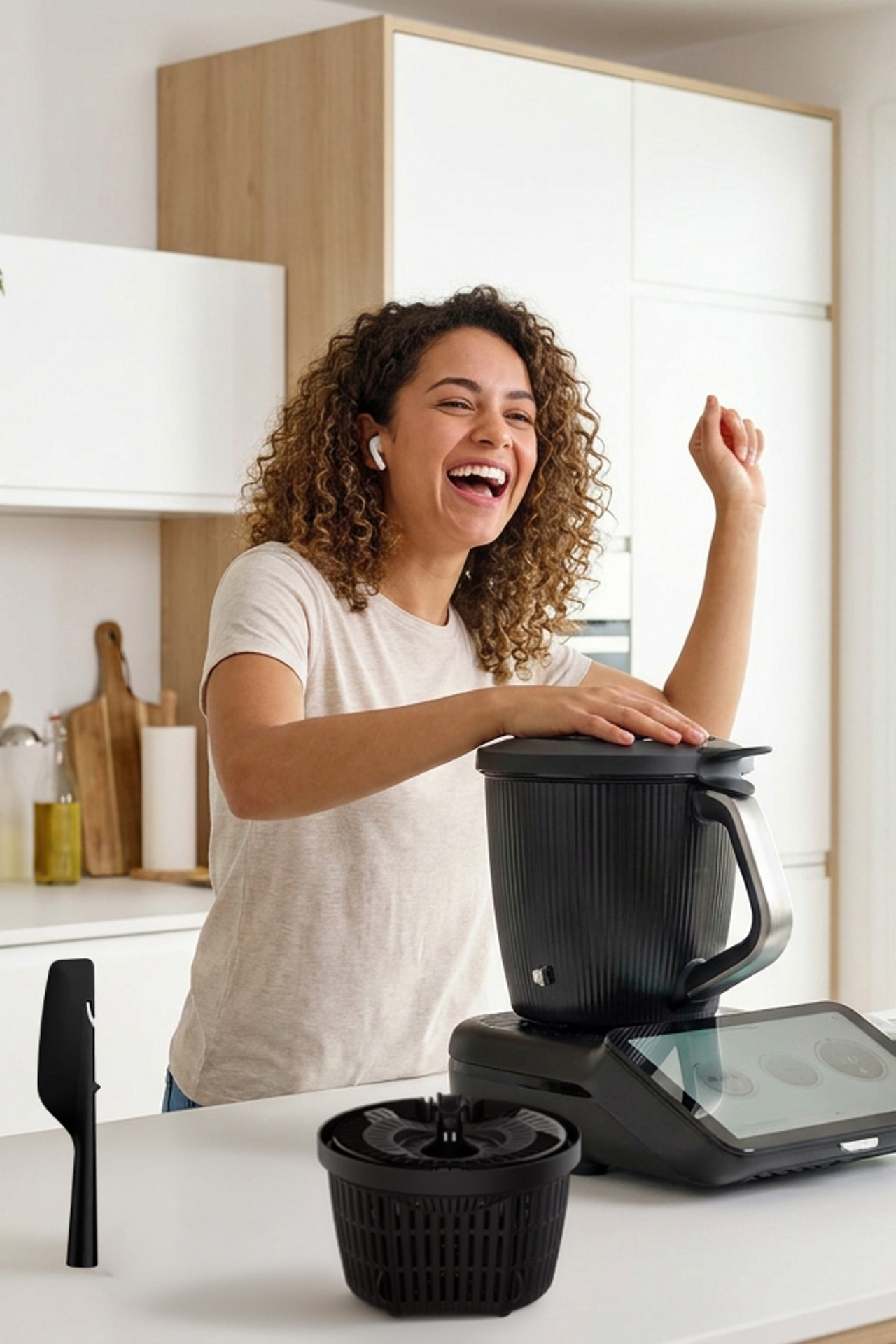 Mujer en cocina usando Thermomix® TM7, con espátula negra y cesta mezcladora negra visibles en la encimera.