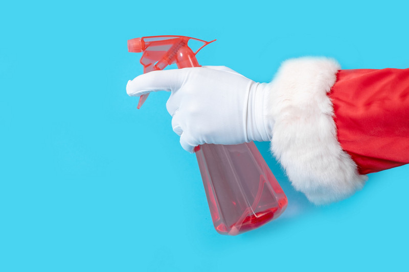 Santa Claus holds red dispenser on the blue background. Hands of Santa with sprayer for cleaning.