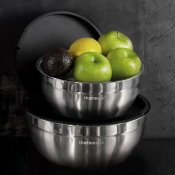Duas tigelas de inox Bimby uma com maçãs verdes um limão e um abacate empilhadas sobre superfície escura