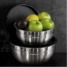 Duas tigelas de inox Bimby uma com maçãs verdes um limão e um abacate empilhadas sobre superfície escura