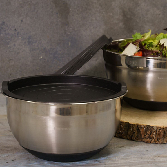 Tigelas de aço inox uma com tampa ao lado de tigela com salada sobre tábua de madeira