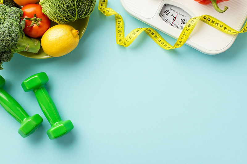 Weight loss concept. Top view photo of plate with vegetables pepper cabbage lemons cauliflower tomato dumbbells scales and tape measure on isolated pastel blue background with copyspace