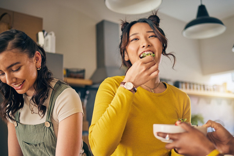 Women, friends and eating healthy food in home for bonding, nutrition and happy lunch together. Fruit diet, sharing and wellness, fresh summer friendship and girls in kitchen with smile at party