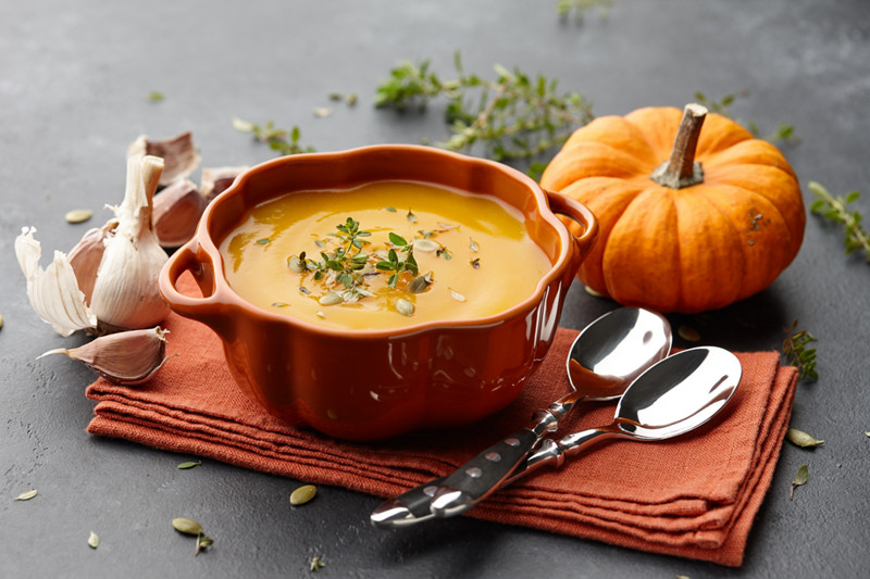 Pumpkin soup with thyme herb, cream and pumpkin seeds served in orange pumpkin shaped bowl