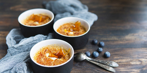 Homemade creme brulee - traditional french vanilla cream dessert with caramel decor, caramelised brown sugar on top in black baking dishes, wooden  table, grey textile and spoons. Copy space.