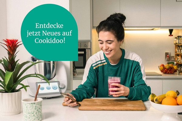 Frau in Küche entdeckt via Handy Neues auf Cookidoo®! 