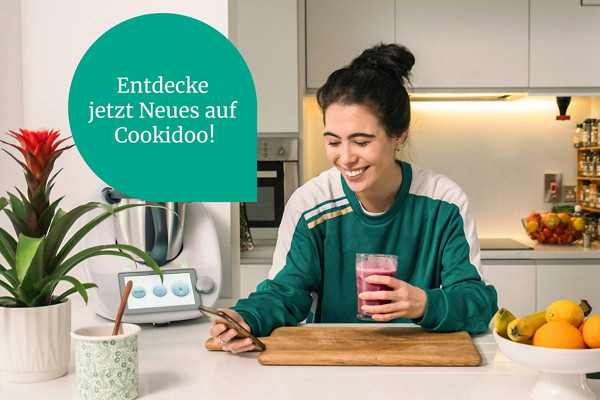 Frau in Küche entdeckt via Handy Neues auf Cookidoo®! 