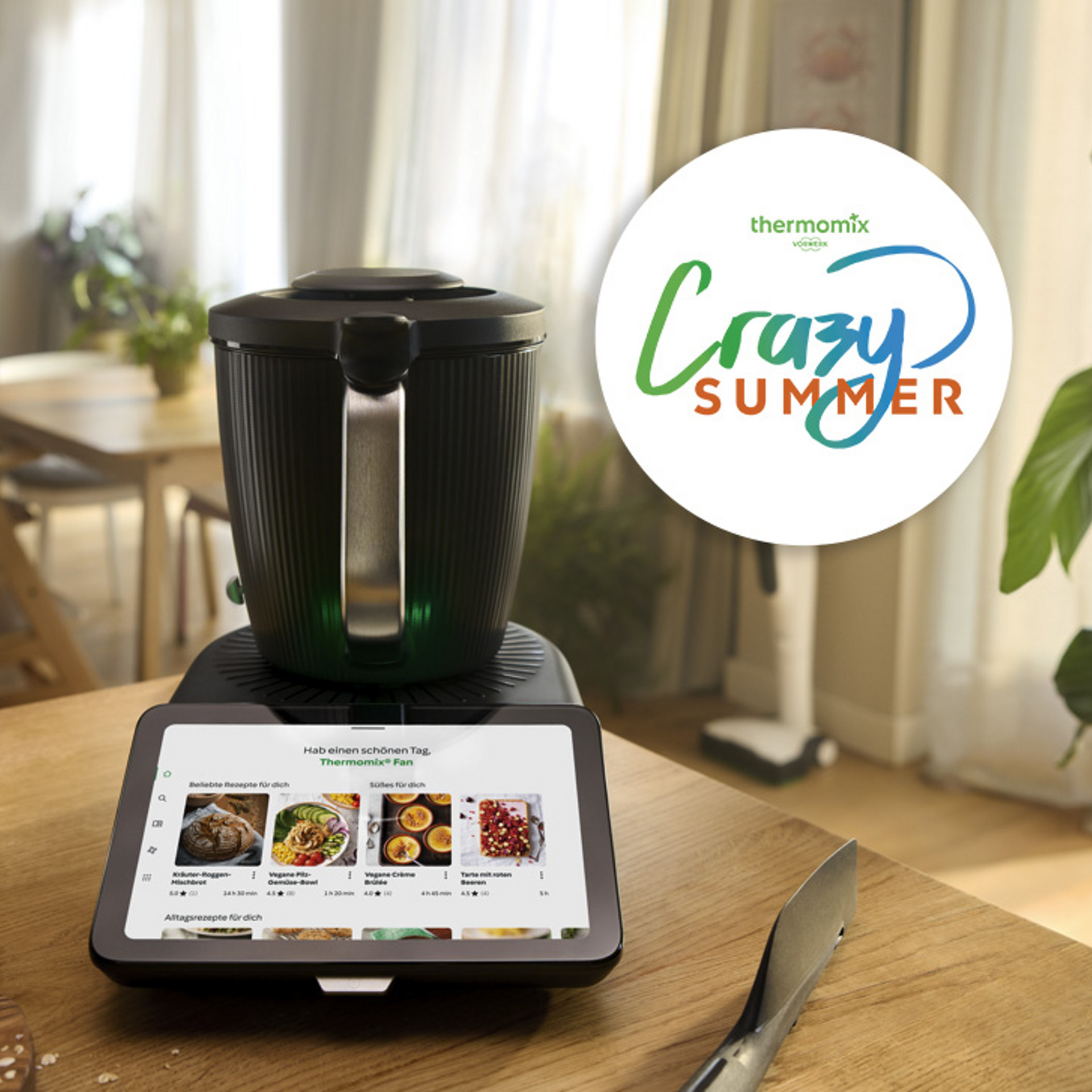 Thermomix® TM7 auf einer Küchenarbeitsplatte mit Touchscreen, Obst, Milchkrug und Crazy Summer Aktionslogo.