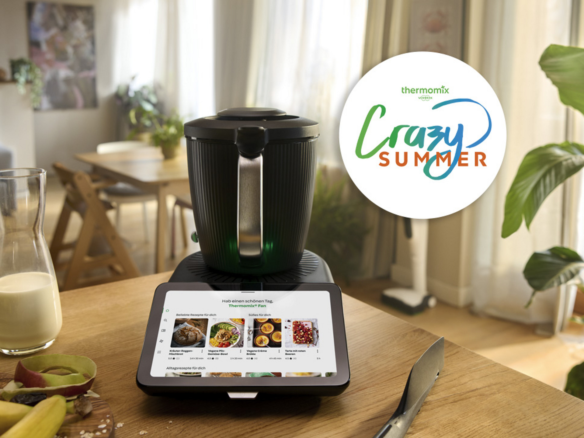 Thermomix® TM7 auf einer Küchenarbeitsplatte mit Touchscreen, Obst, Milchkrug und Crazy Summer Aktionslogo.