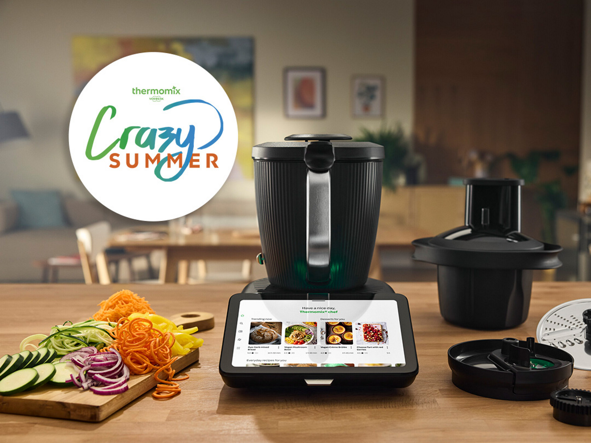 Thermomix® TM7 und Thermomix® Gemüse Styler auf Küchentisch mit geschnittenem Gemüse und "Crazy Summer" Logo im Hintergrund.
