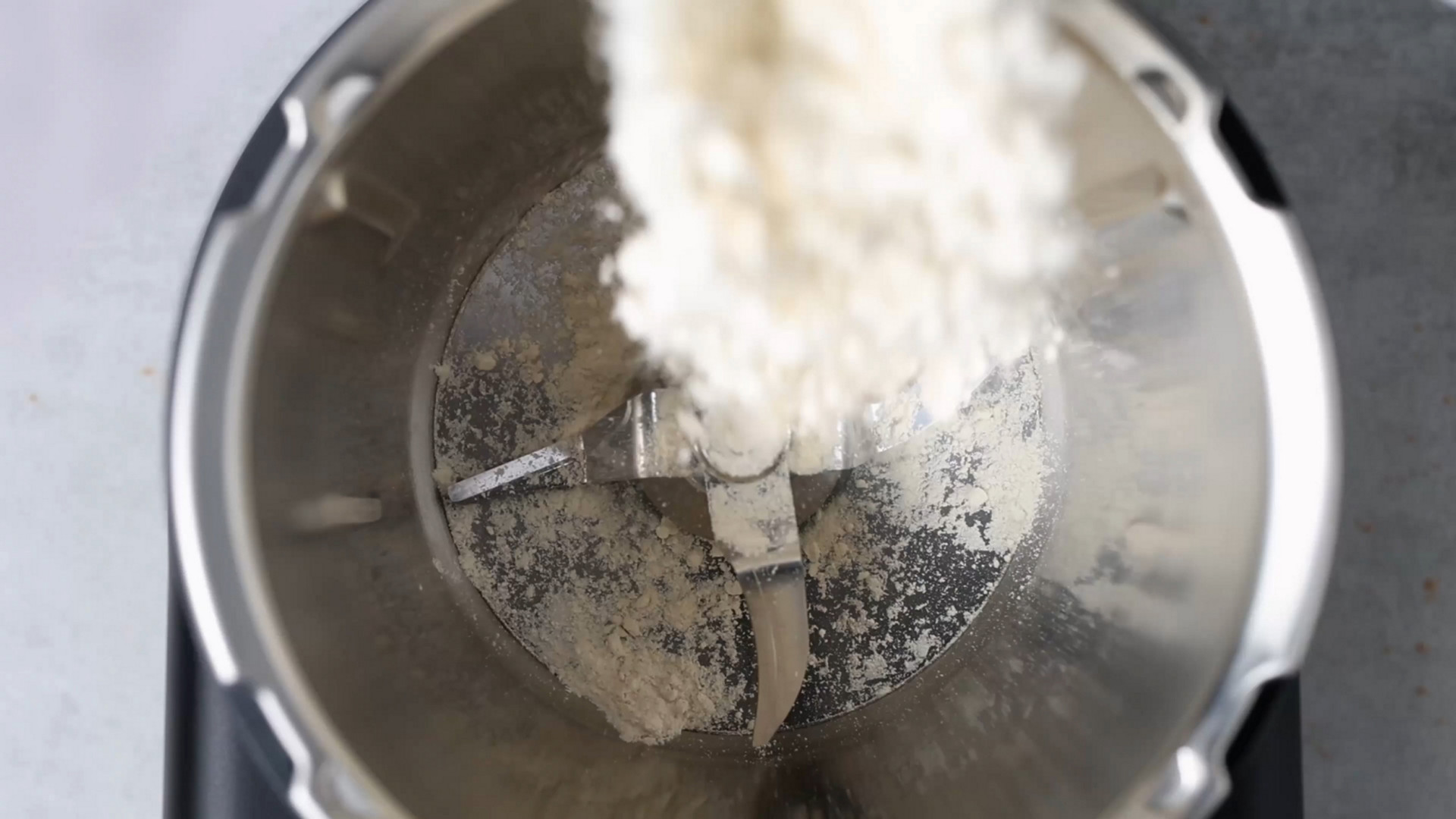Mehl wird von oben in den Mixtopf eines Thermomix® TM6 mit sichtbarem Mixmesser eingefüllt.
